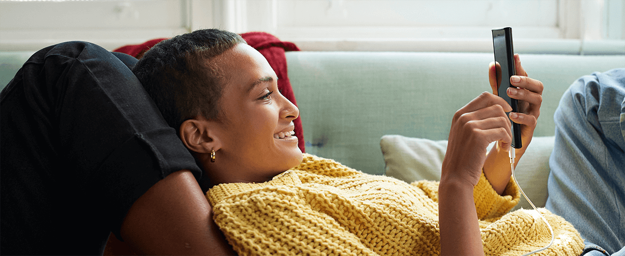 a woman smiling while looking at her phone on the sofa