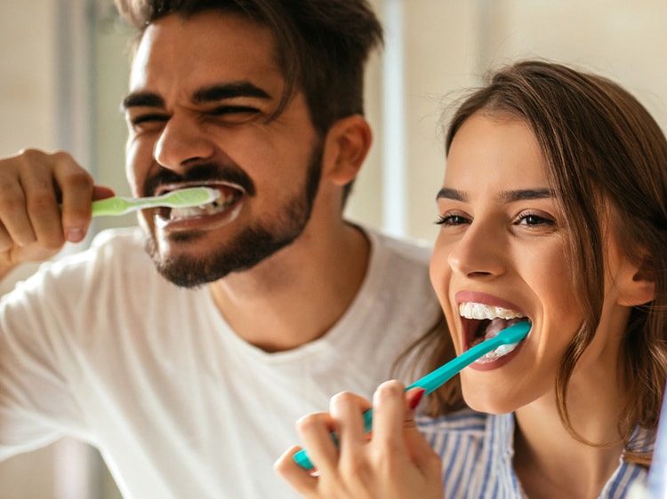 Imagen de una pareja joven en el espejo cepillándose los dientes