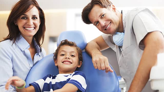 Dentista sonriendo atendiendo a un niño junto a su madre