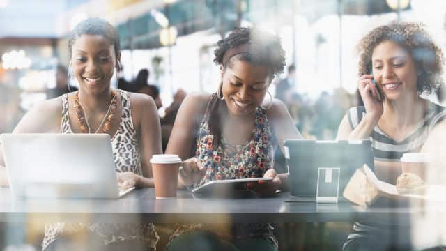 Tres jovenes sonriendo mientras trabajan y toman un cafe