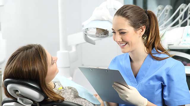 Dentist holding a clipboard and talking to the patient.