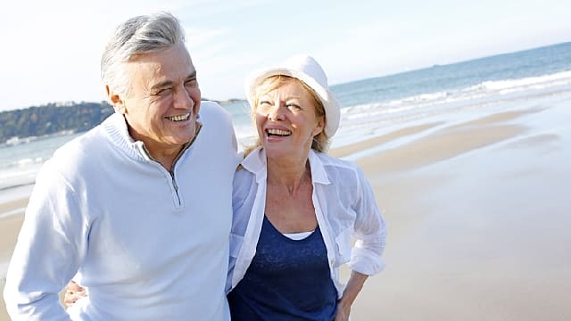 a senior couple are walking along the beach after TMJ treatment