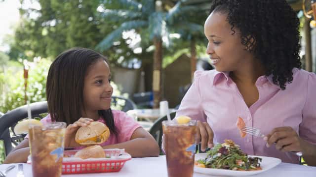 A mother and daughter smiling brightly sitting down enjoying lunch