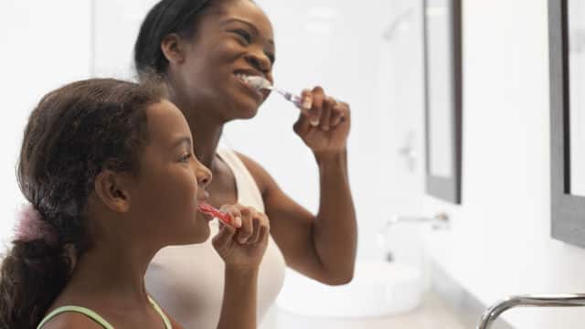 mother and daughter smiling while brushing their teeth with Colgate toothbrush